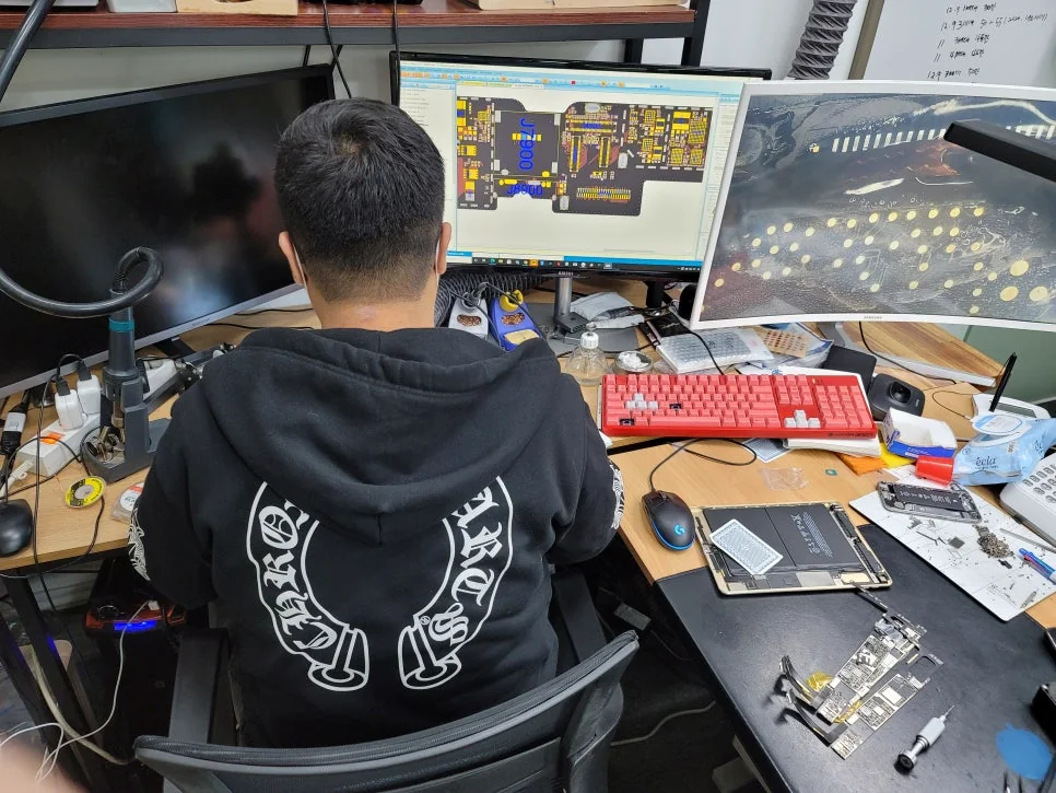 Student studying an iPhone board schematic at the repair bench, FIXSTORY ACADEMY