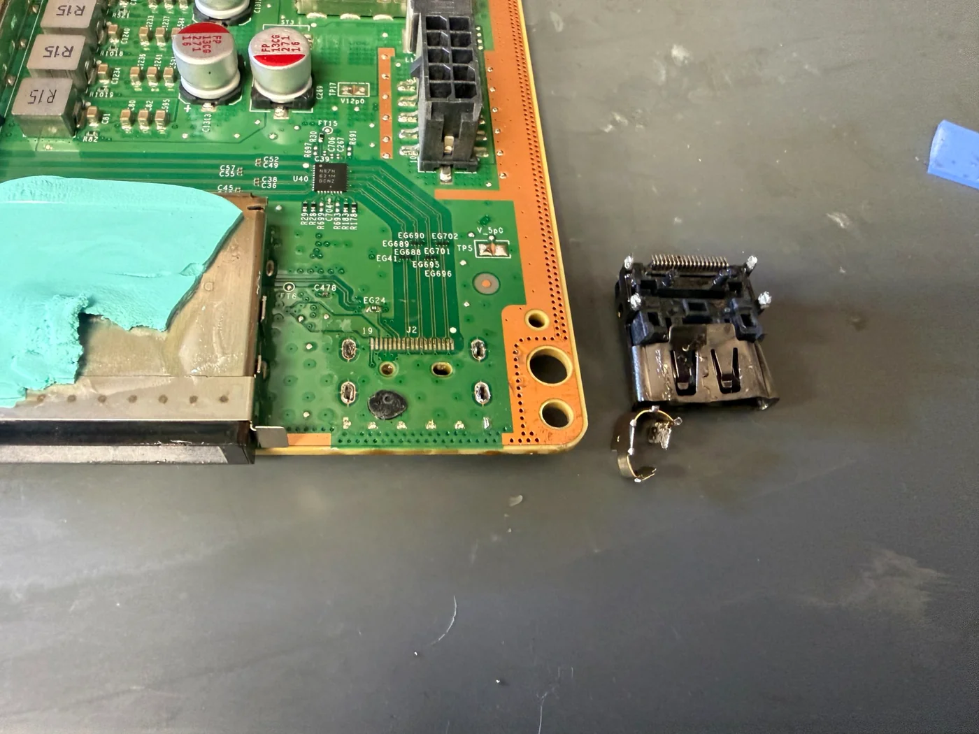 Xbox Series X mainboard with the HDMI pads cleaned, the old port and its broken shield piece beside it