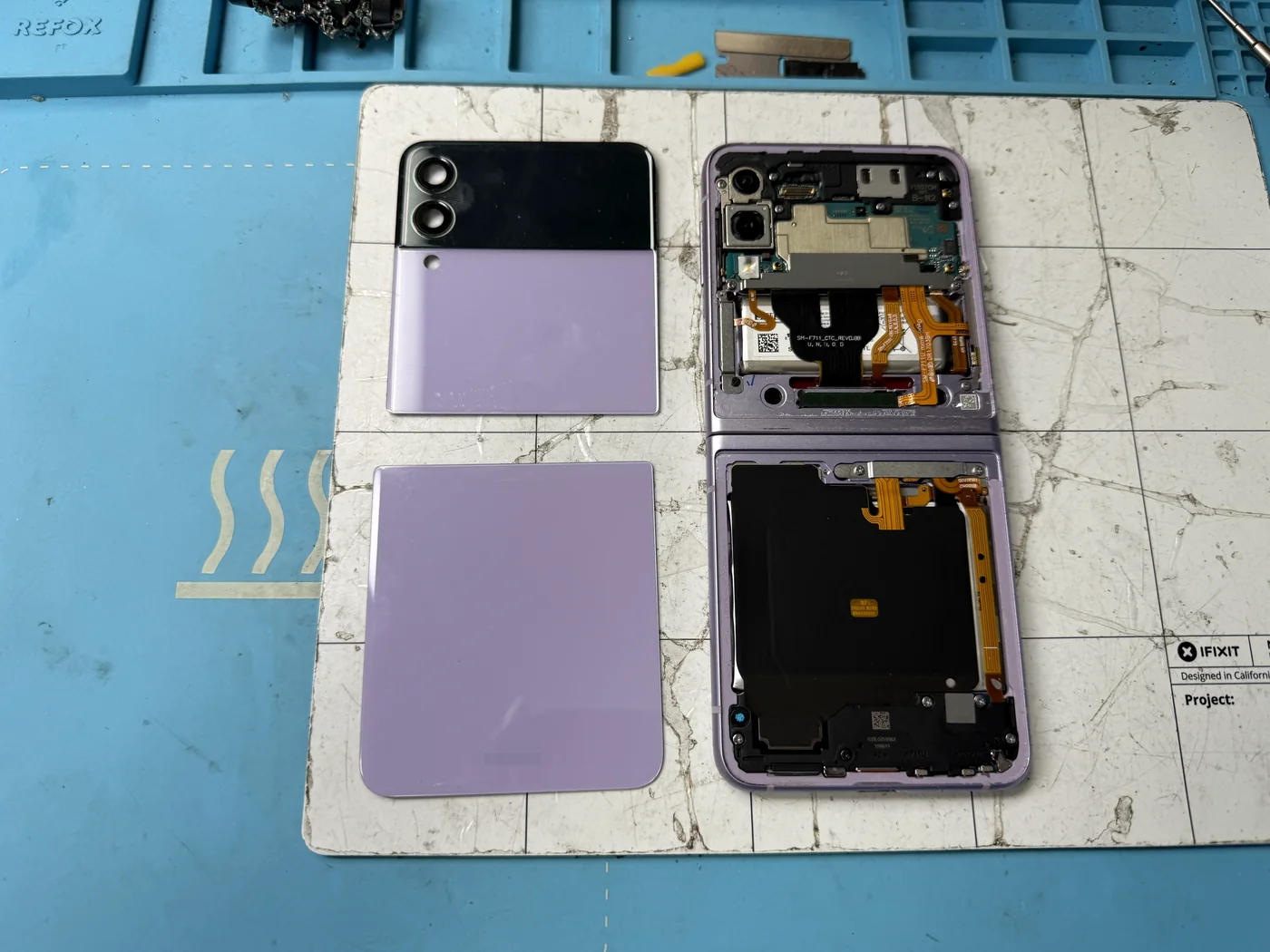 Galaxy Z Flip 3 with both back glass panels removed, exposing the battery, board and folding screen flex cables