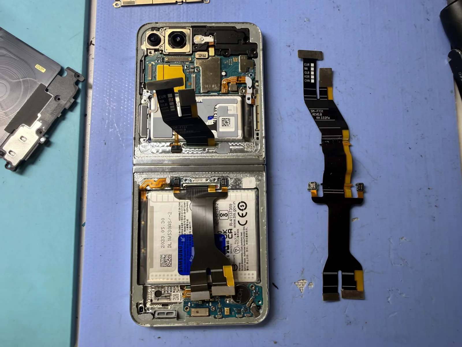 Galaxy Z Flip 5 opened on the bench with the hinge flex cable removed and laid beside the phone