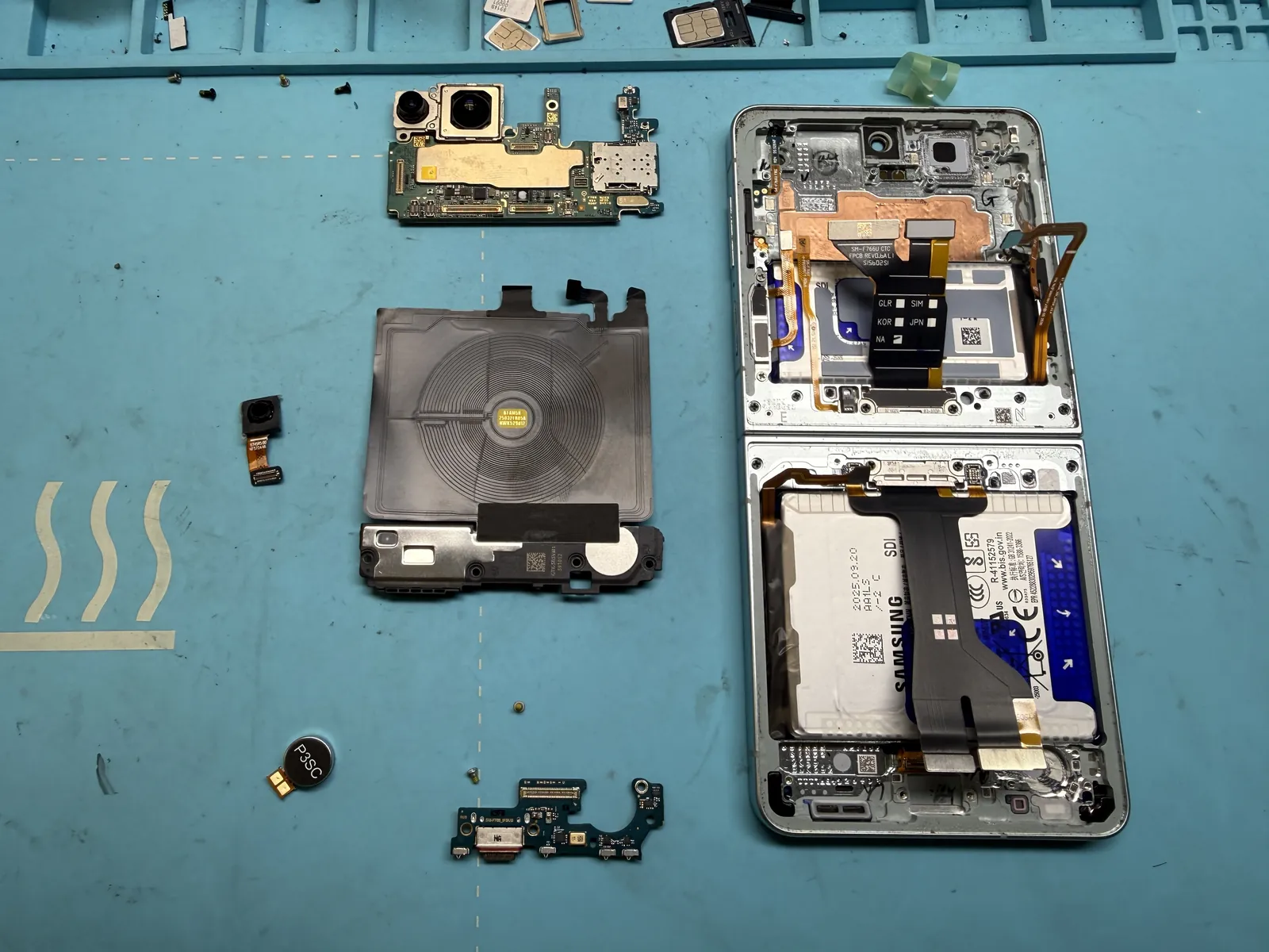 Every internal part removed from the broken Galaxy Z Flip 7 frame, laid out on the mat
