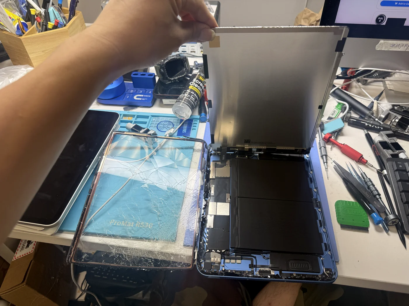 Original LCD lifted out of the iPad 11-inch (2025), cracked digitizer beside it, battery and board exposed