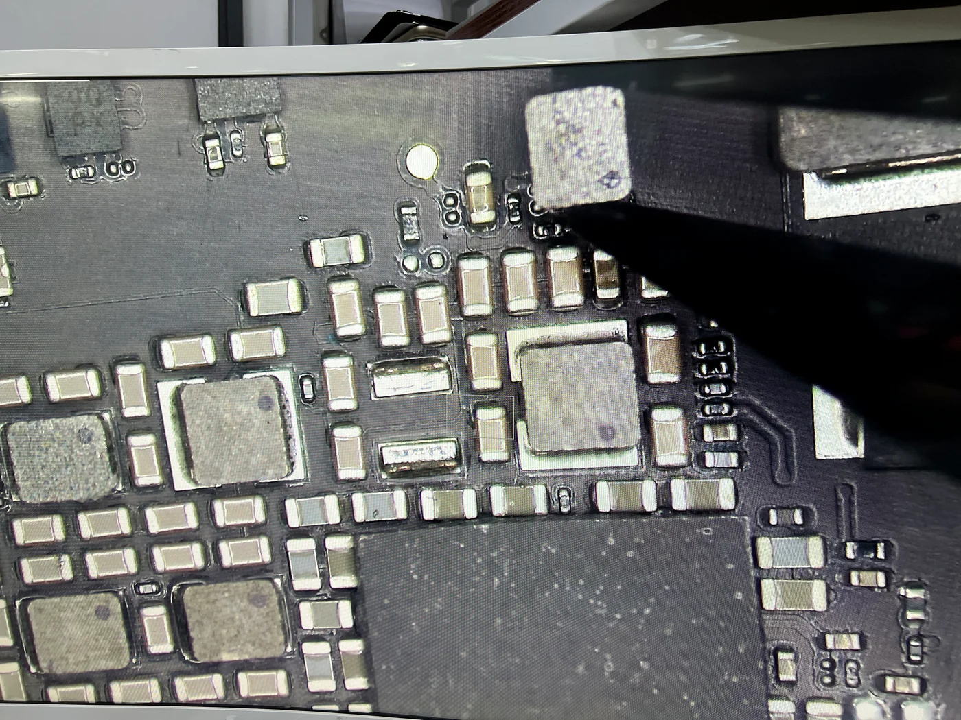 Microscope view of the iPad Pro 10.5 logic board with the loose power coil lifted off by tweezers, leaving its empty pads
