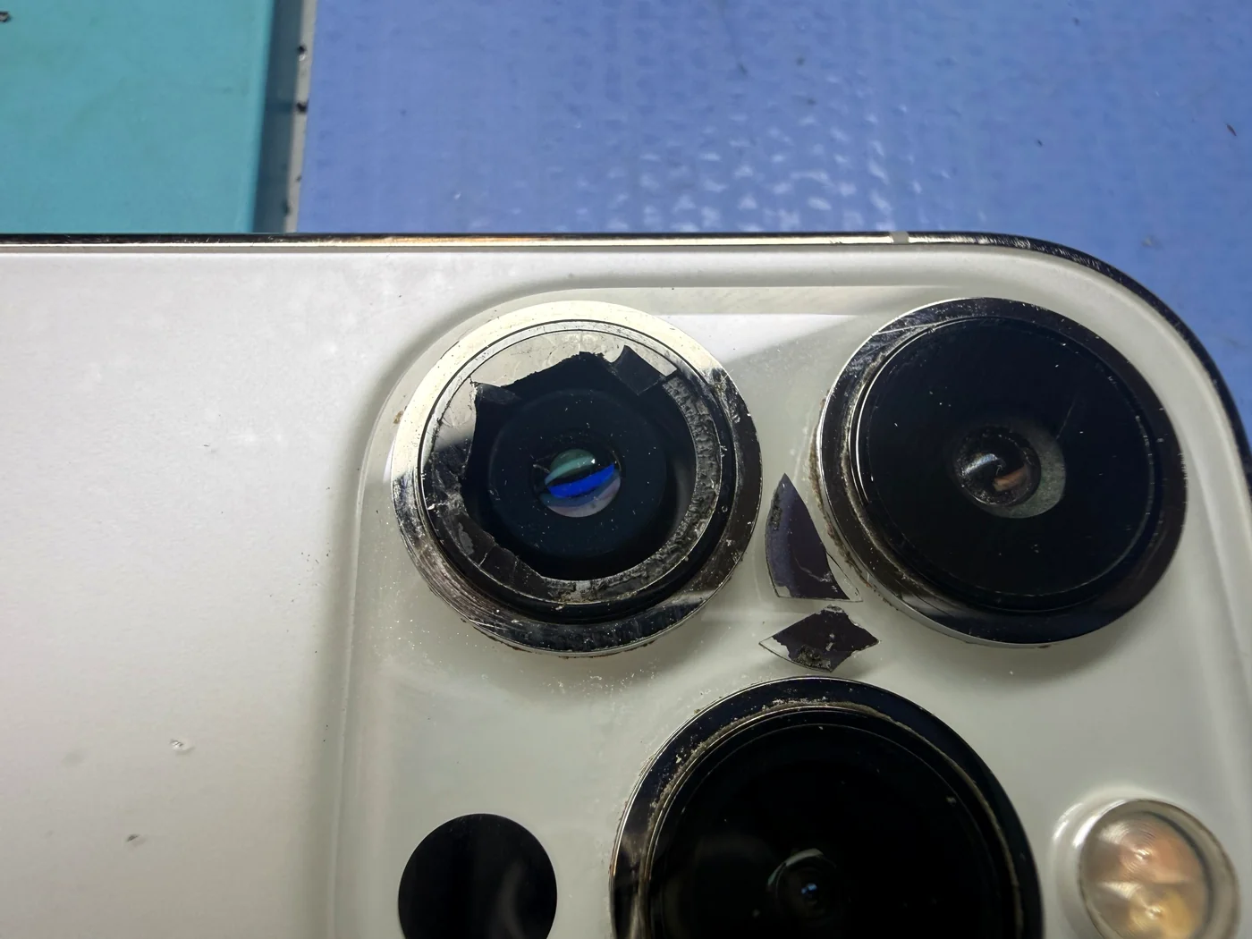 Shattered iPhone 14 Pro camera lens cover glass being removed piece by piece