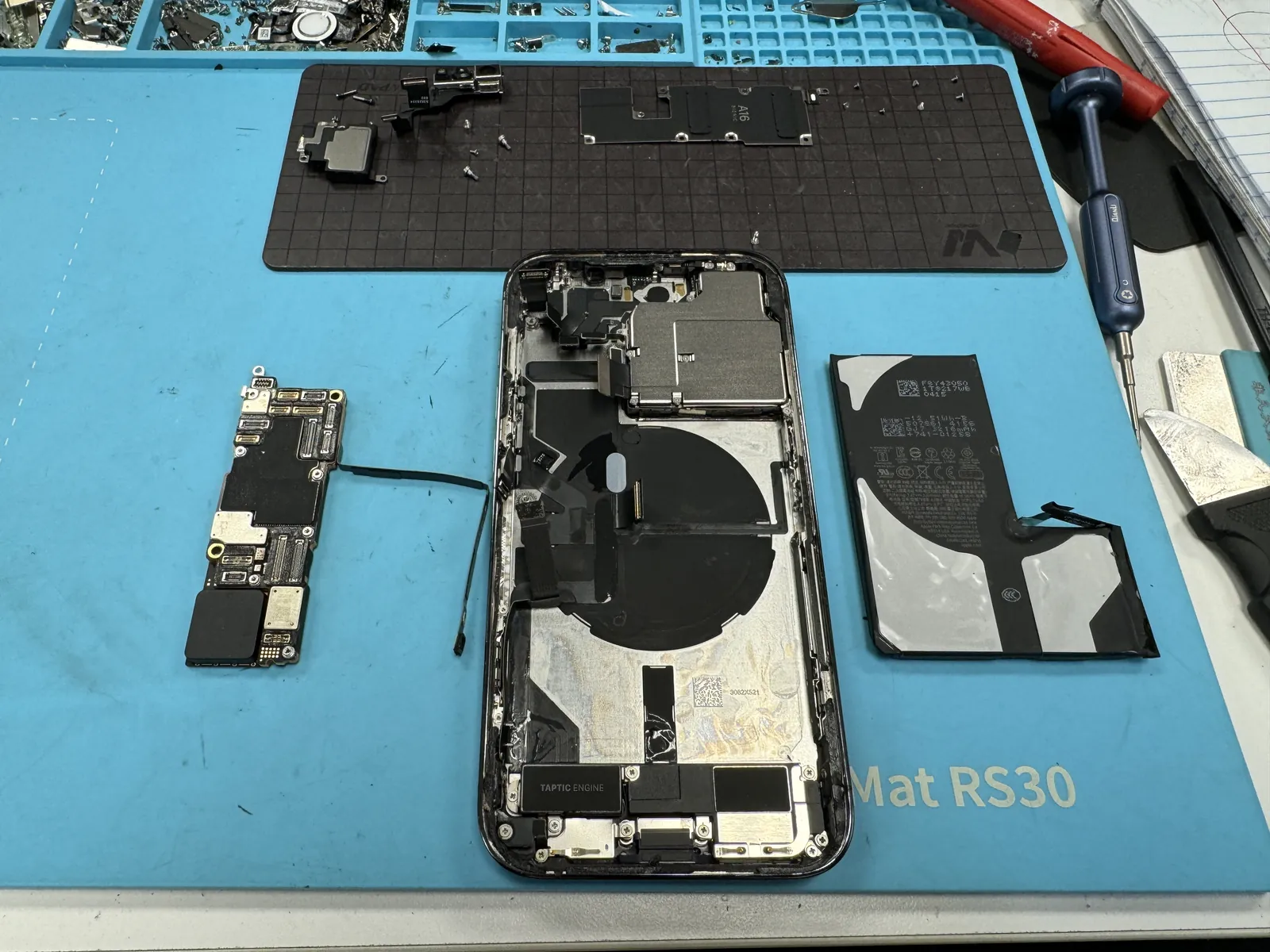 iPhone 14 Pro fully torn down on the bench with the logic board and battery removed from the housing