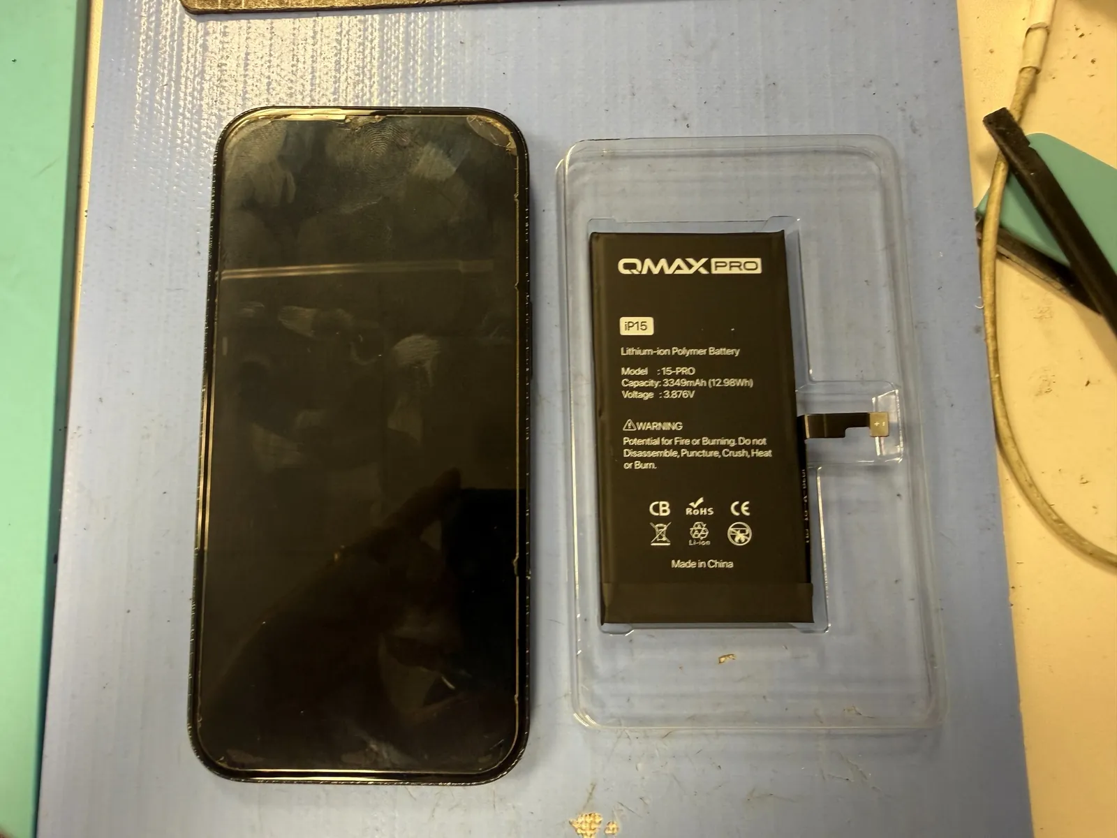 iPhone 15 beside a new aftermarket battery before replacement