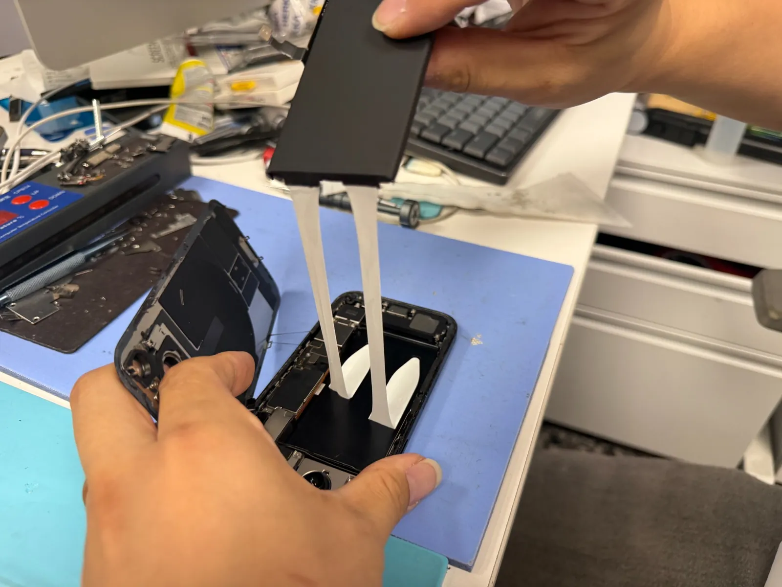 Original iPhone 15 battery being released by pulling the adhesive strips