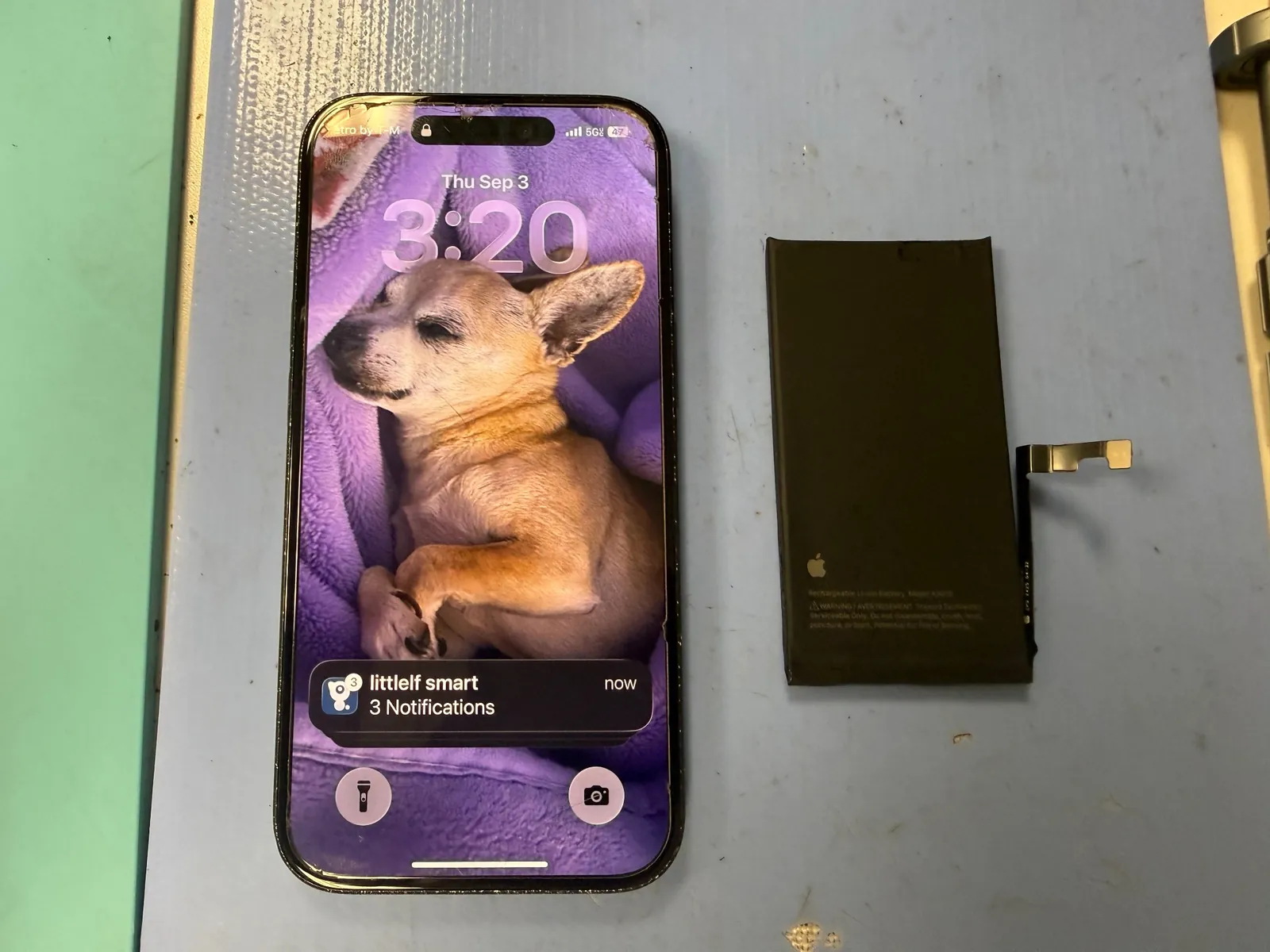 iPhone 15 powered on after battery replacement beside the removed Apple battery