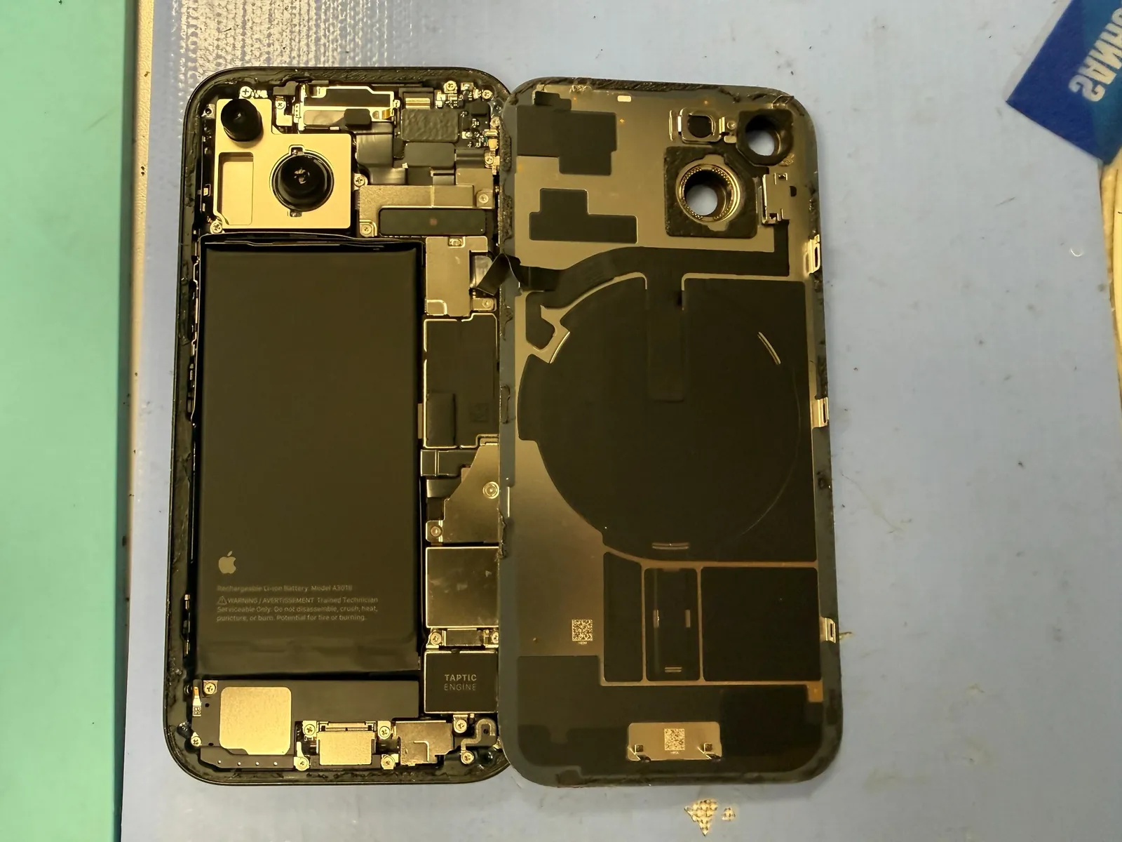 iPhone 15 opened from the rear with the back glass lifted for battery access