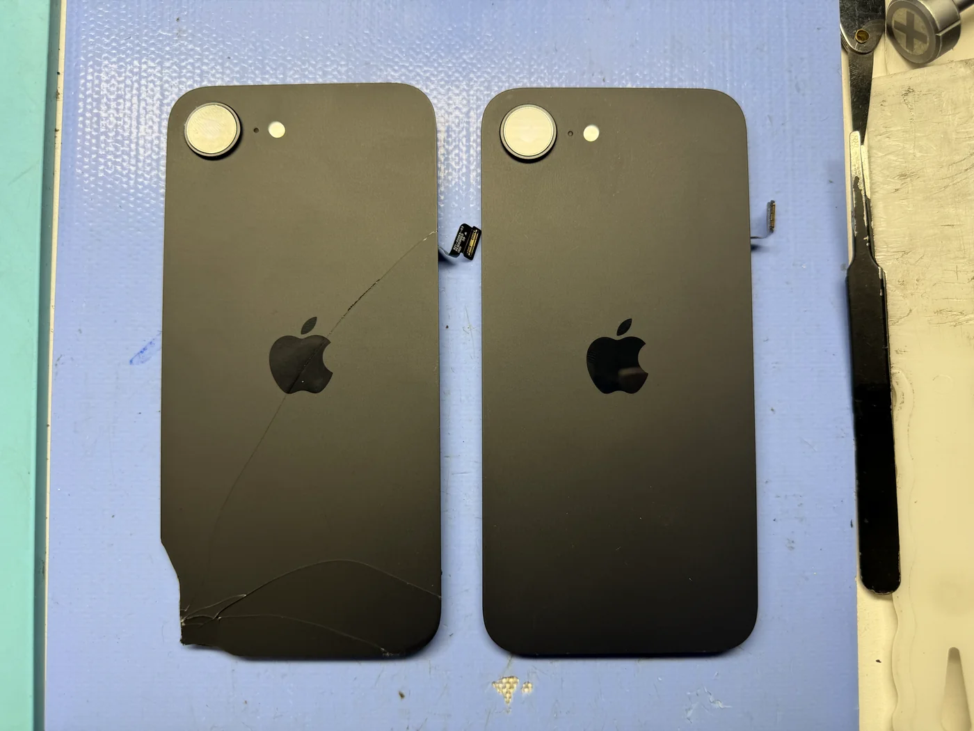 Cracked original iPhone 16e back glass beside the new genuine replacement