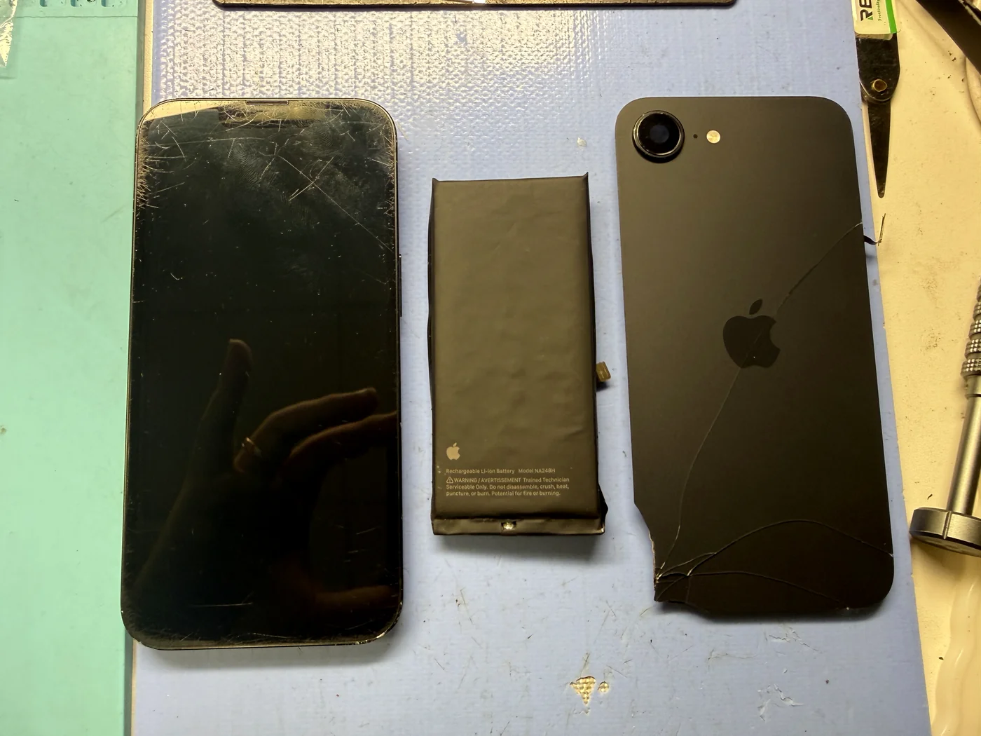 Swollen battery and cracked back glass laid beside the iPhone 16e body