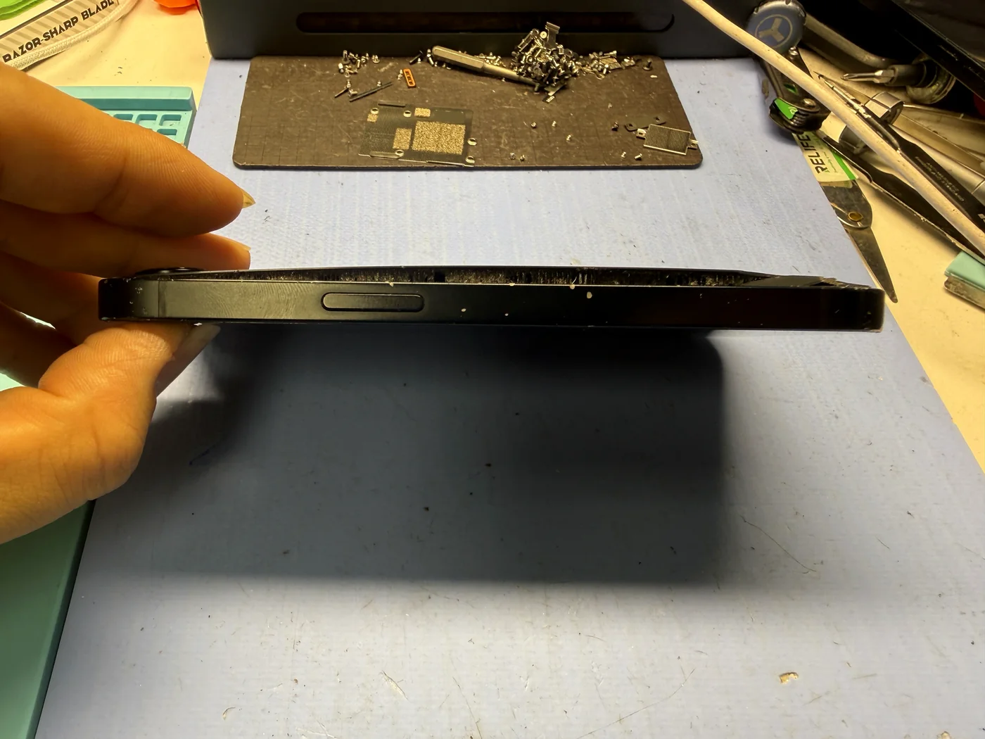 iPhone 16e seen from the side with the back glass lifted off the body by a swollen battery
