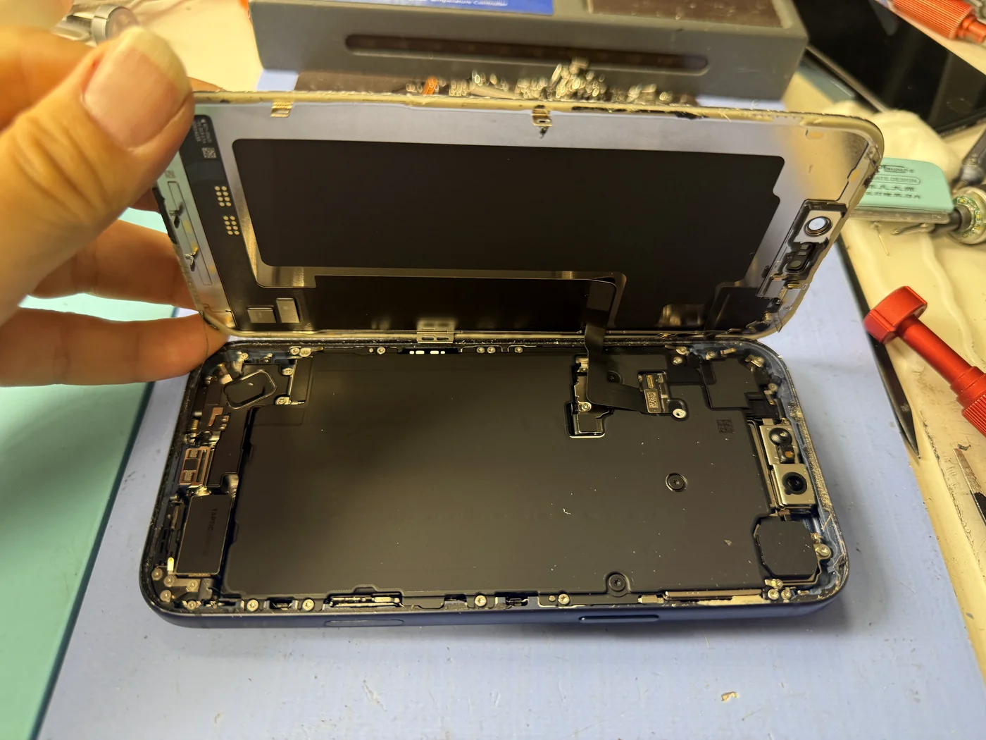 Cracked iPhone 17 Pro Max screen lifted away, showing the two display cables that connect to the logic board