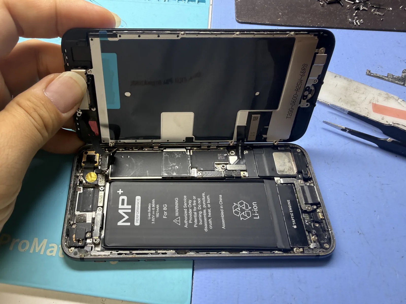 New iPhone 8 screen held open over the frame with a fresh battery installed on the bench