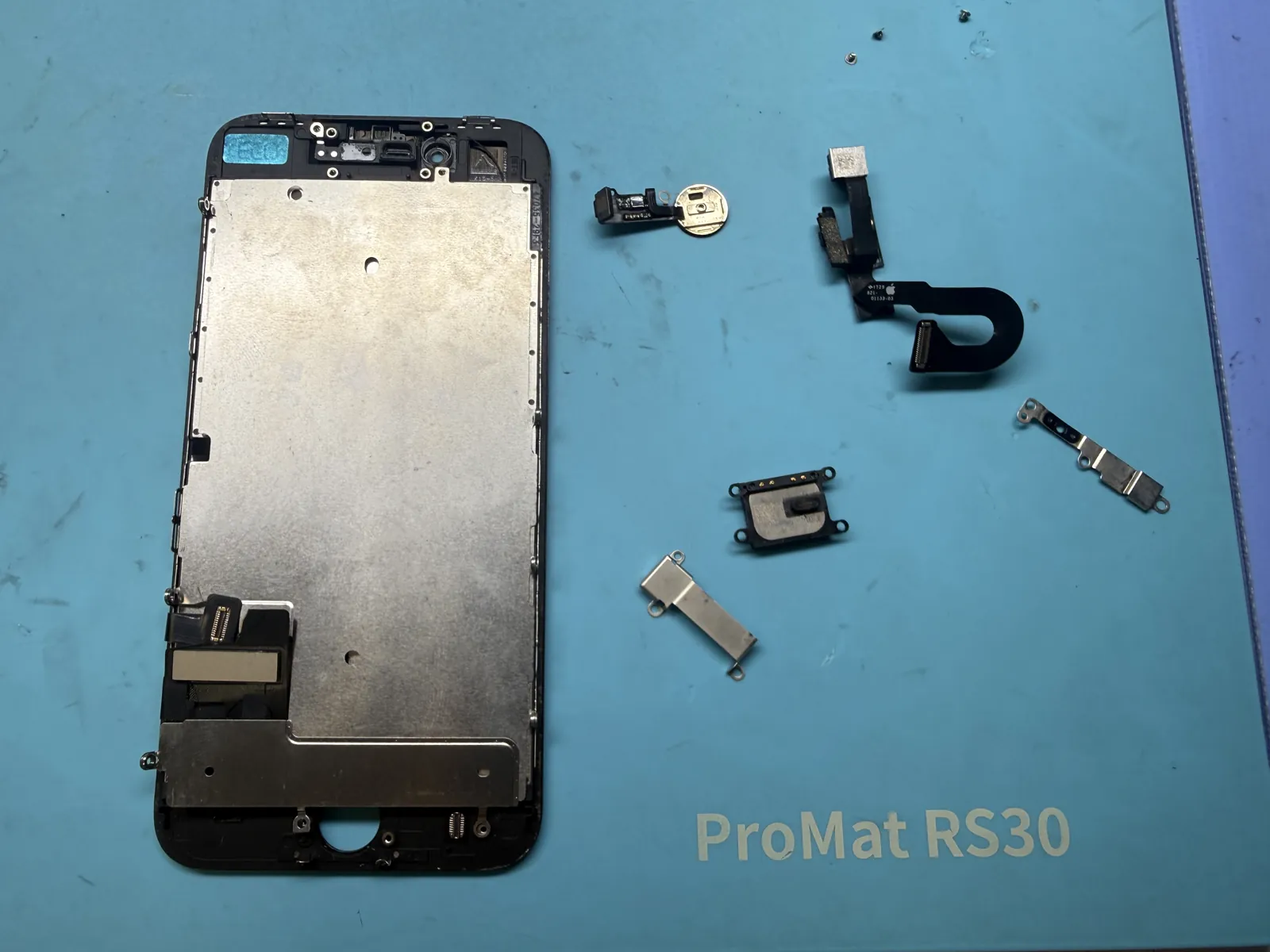 Old iPhone 8 display on the repair mat with the Touch ID home button, front camera flex, earpiece and brackets removed for transfer