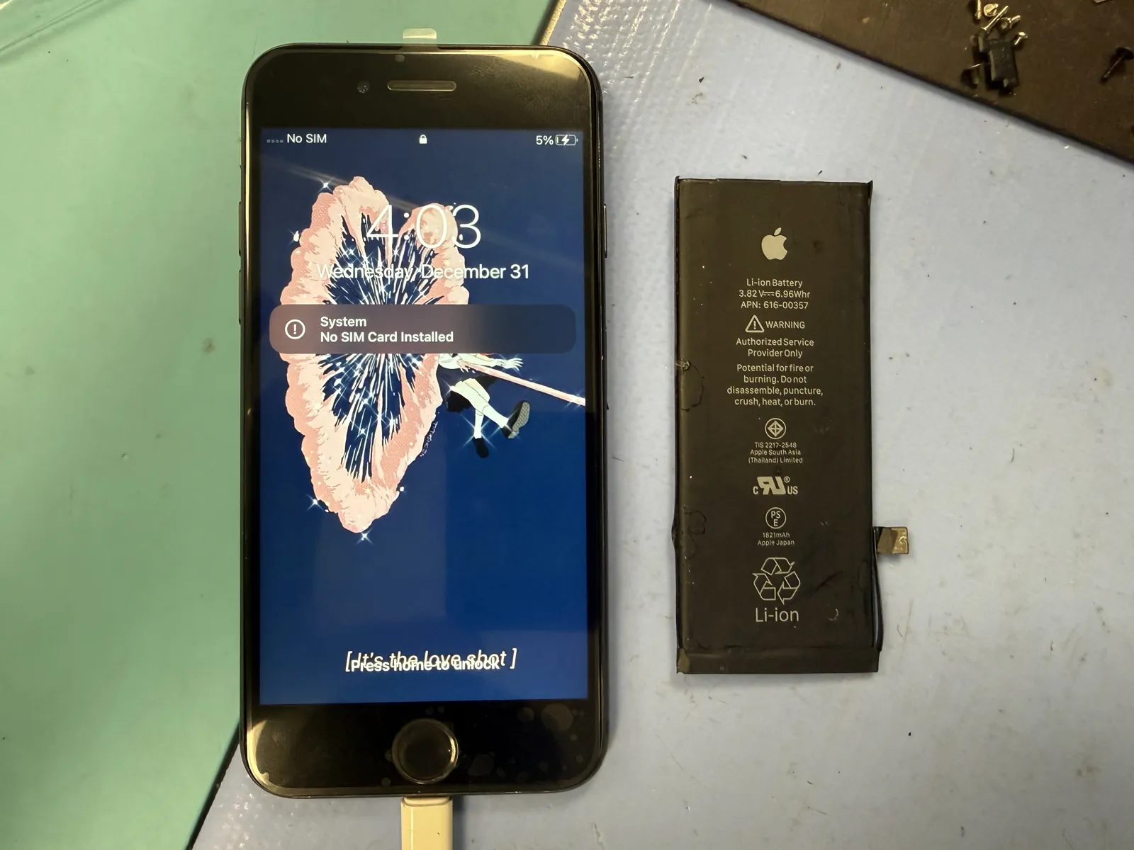 iPhone 8 powered on at the lock screen after screen and battery replacement, with the old Apple battery next to it, at a Los Angeles repair shop