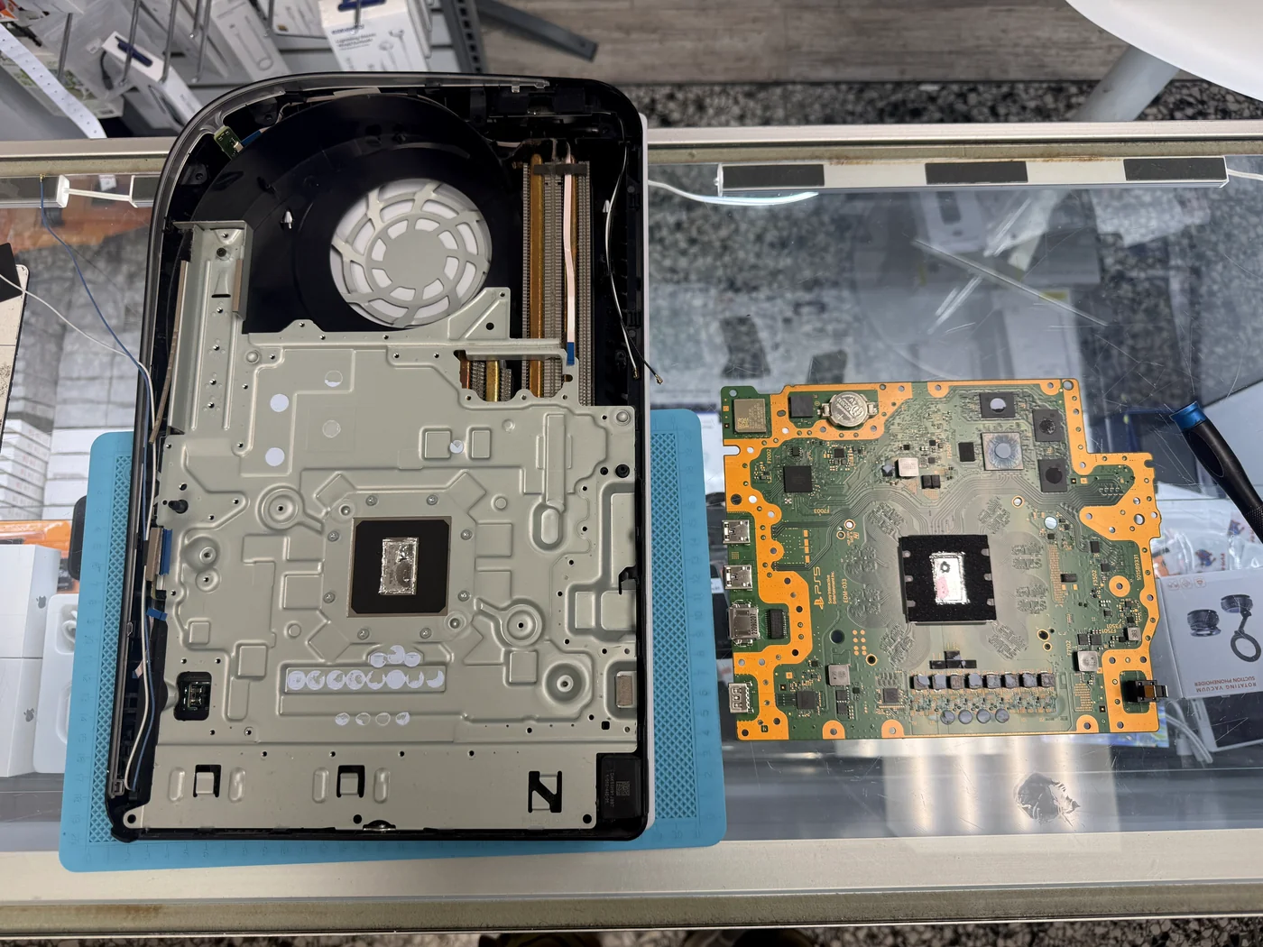 PS5 motherboard removed and set beside the chassis for liquid metal and thermal putty replacement