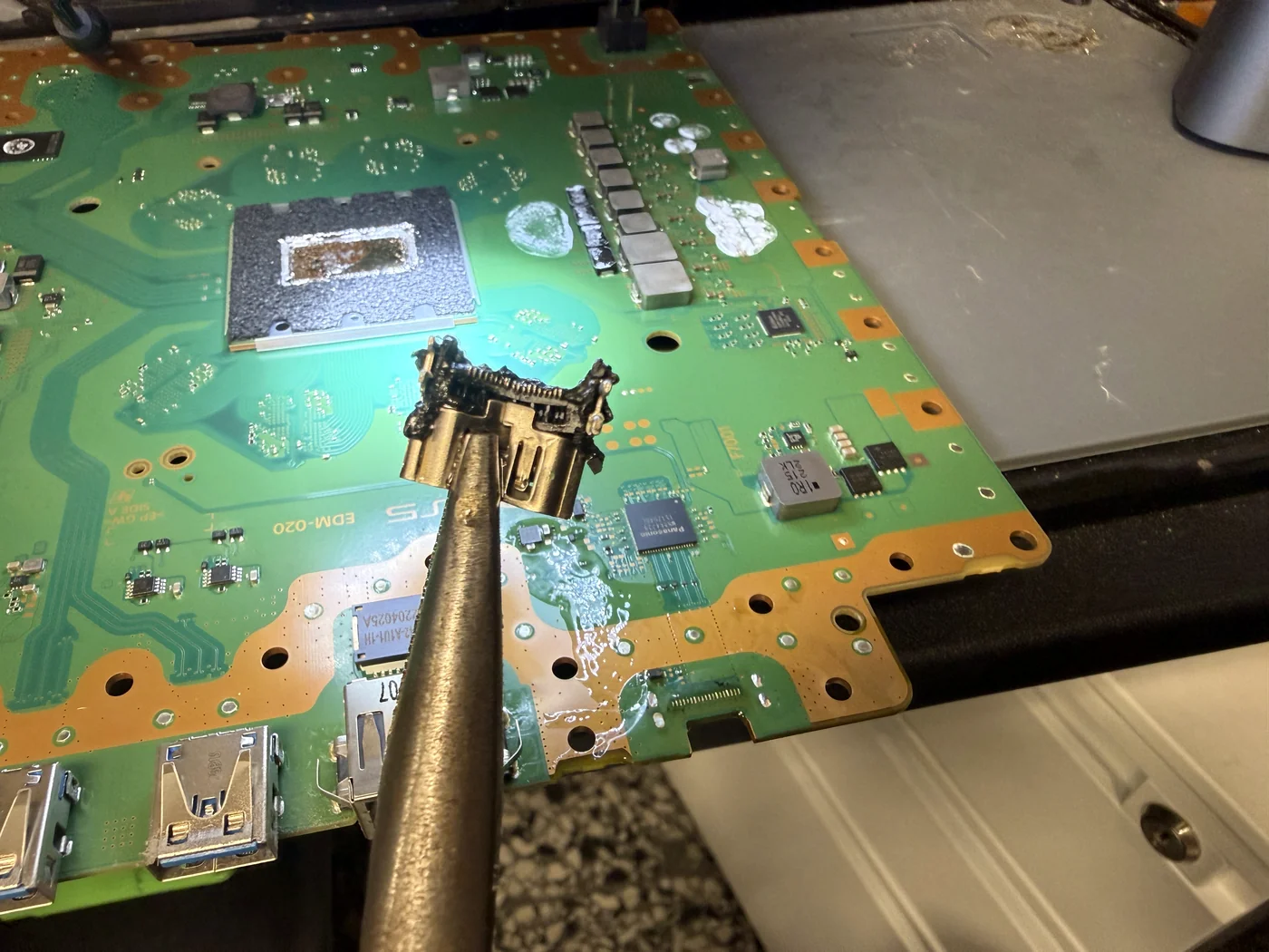 Old PS5 HDMI port lifted off the board with tweezers, pins bent and housing loose