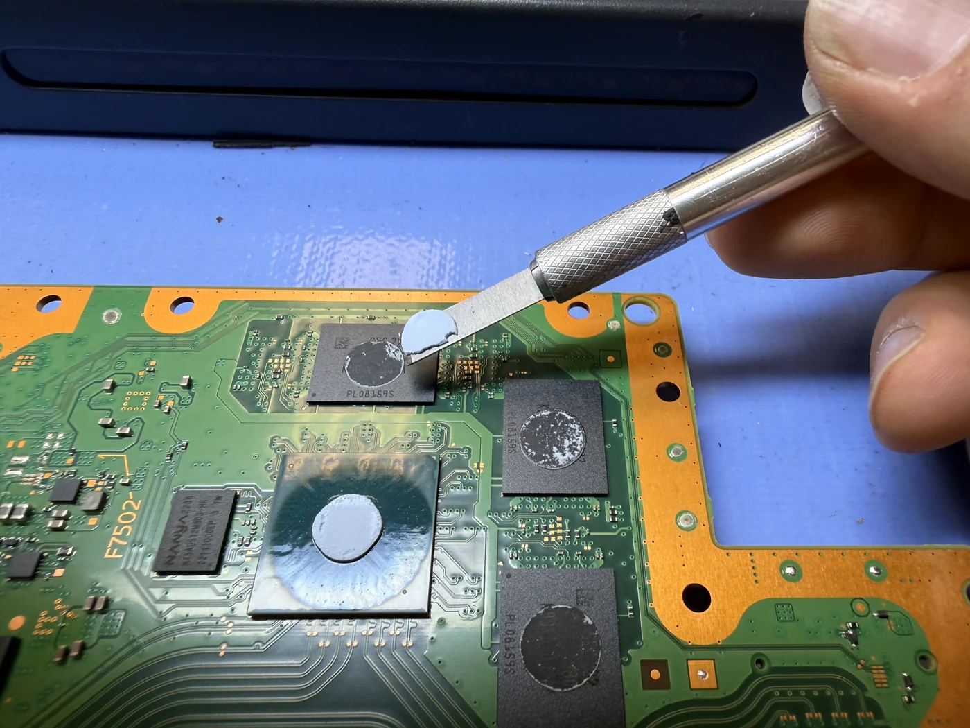 Old thermal putty being lifted off PS5 memory chips with a blade