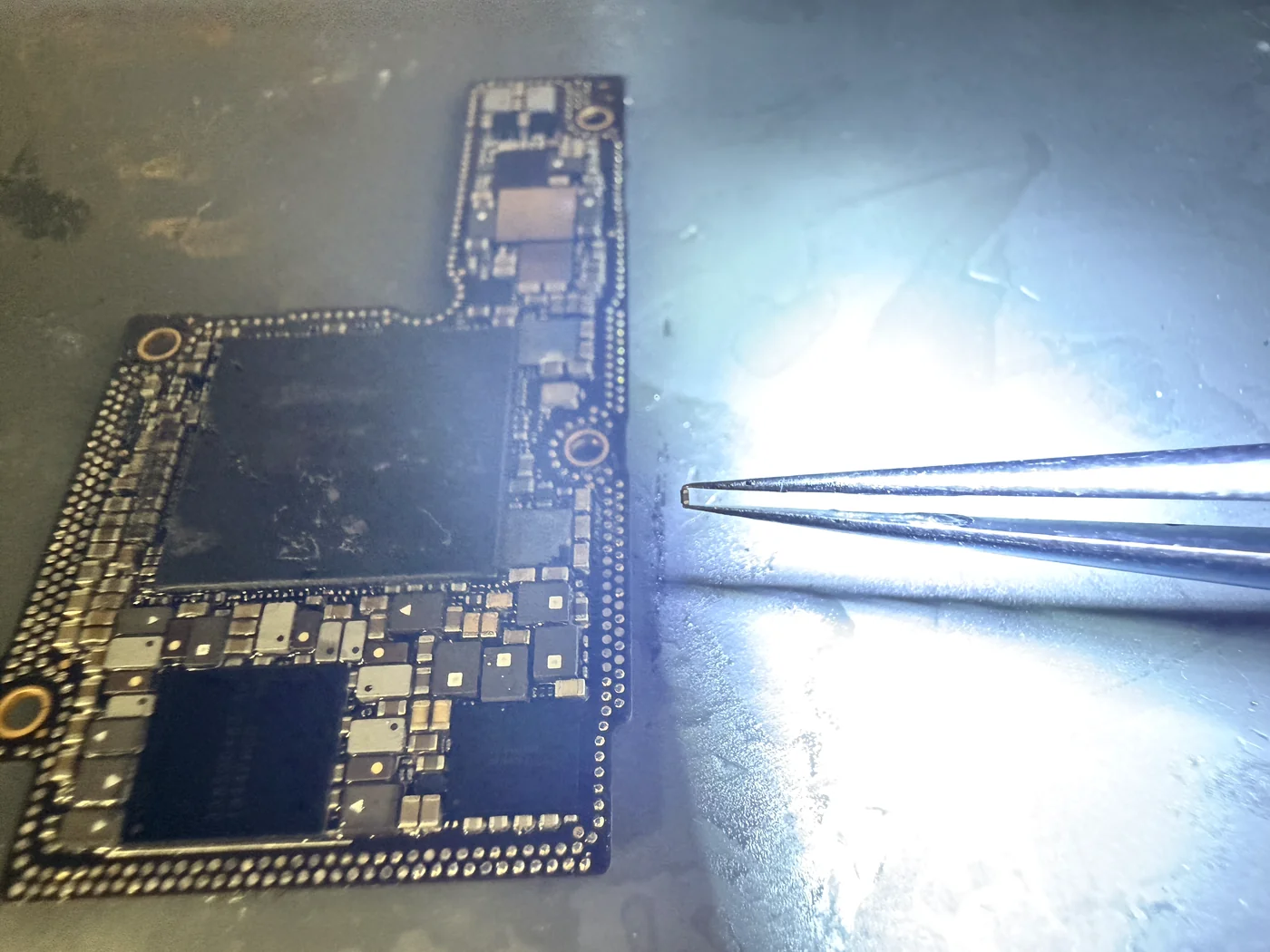 Tiny matching capacitor harvested from a donor iPhone logic board with tweezers for a PS5 repair