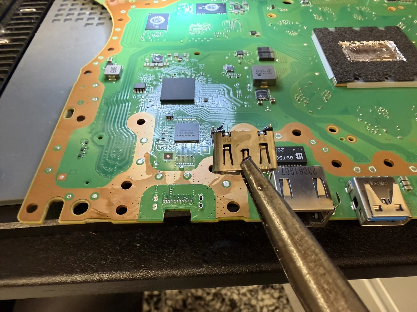 Damaged HDMI port still on the PS5 Slim mainboard, pointed out with tweezers before removal