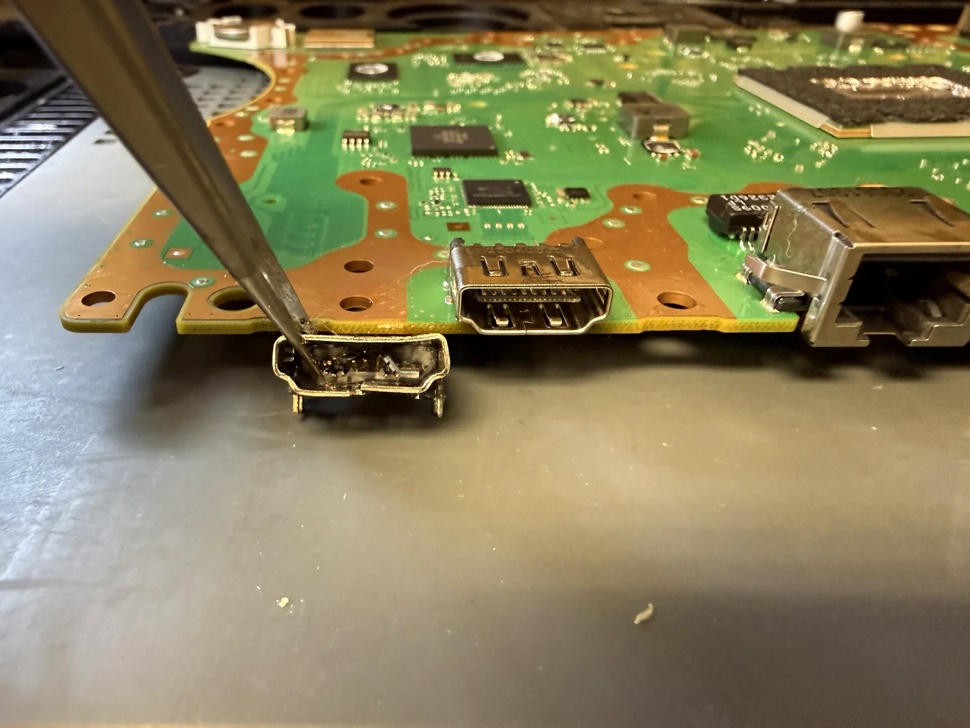 New HDMI port installed on the PS5 Slim mainboard with the old damaged port held in tweezers beside it