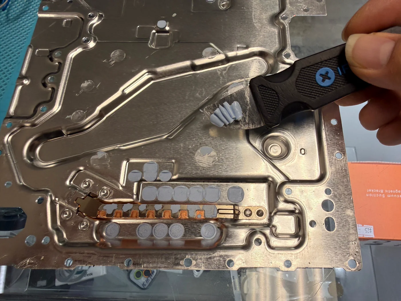 Hardened old thermal putty being scraped off a PS5 Slim heatsink plate with a plastic spudger